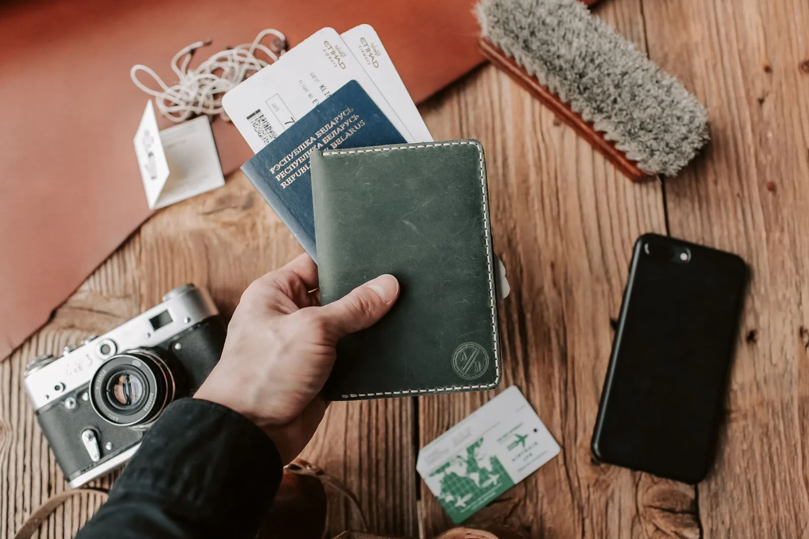 A hand holding a passport beside a phone and tickets
