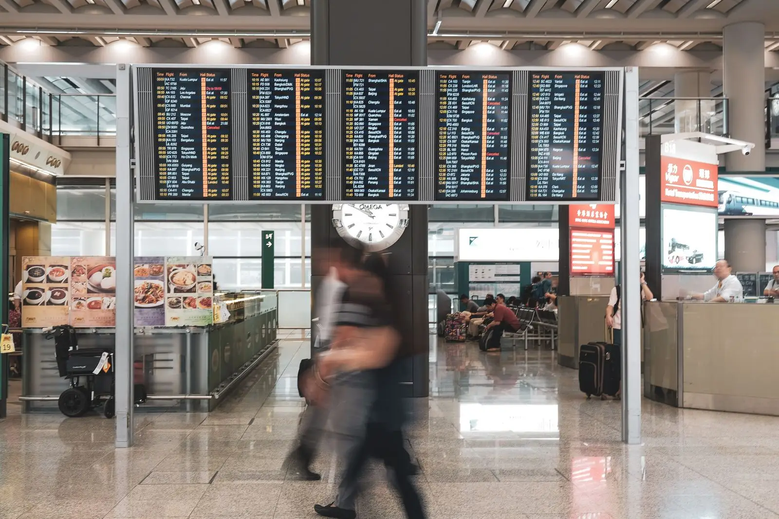 Travellers passing departure screens in an airport terminal