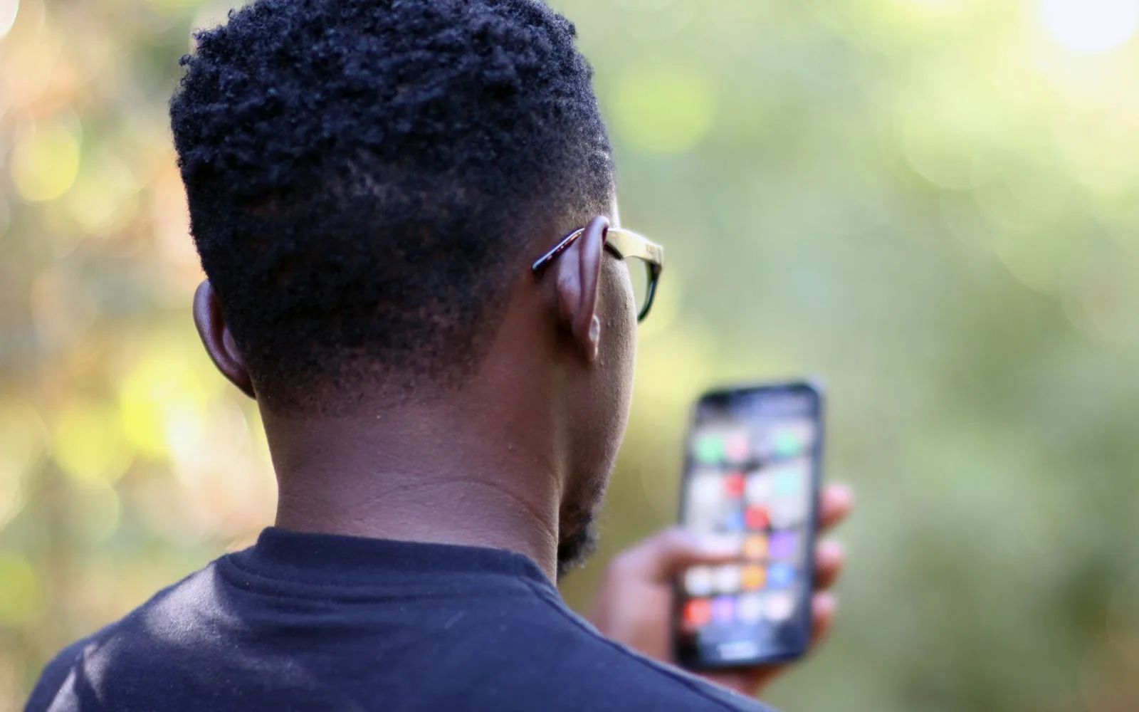 A young man in Kenya holding a smartphone, seen from behind