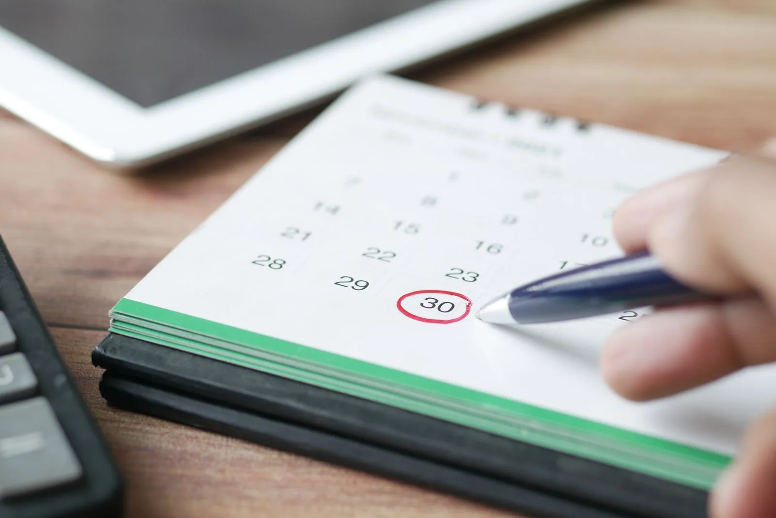 A hand marking a date on a calendar with a pen