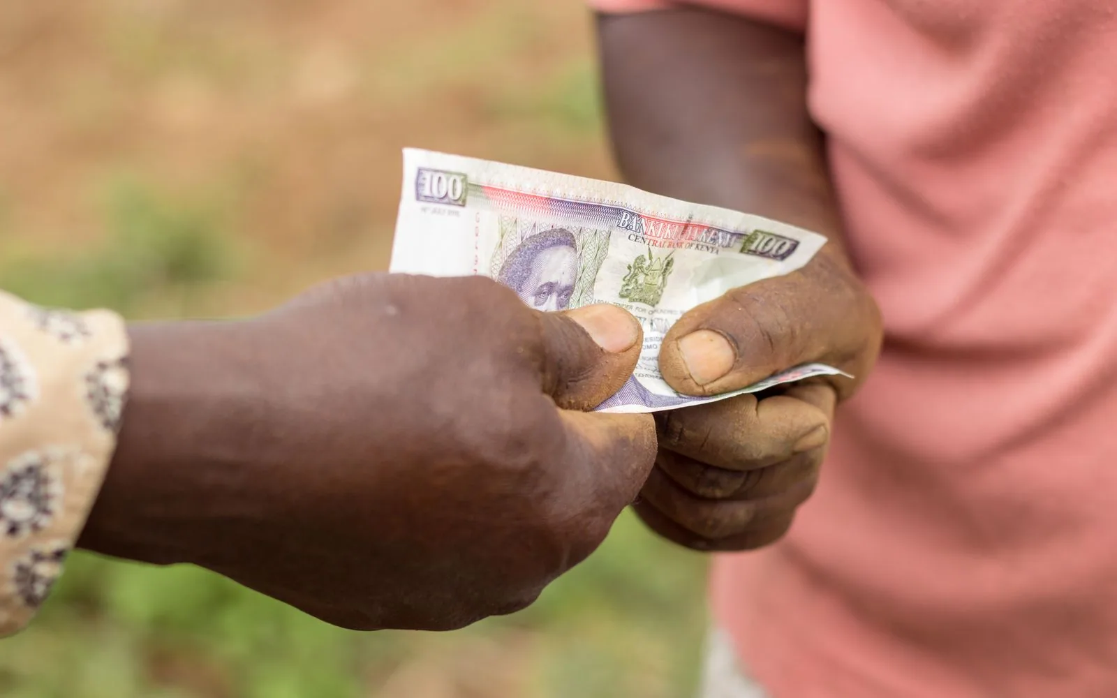 Two people handing over a Kenyan hundred-shilling note outdoors